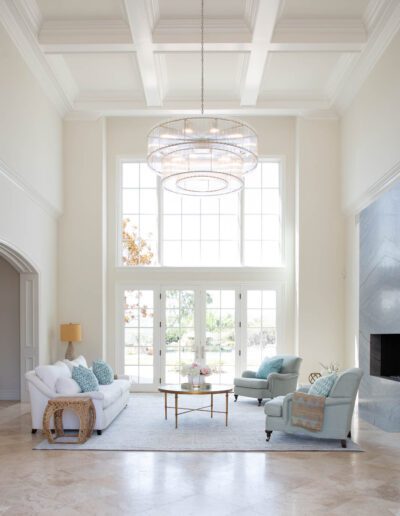 Elegant living room with high ceiling, large windows, and a statement chandelier.