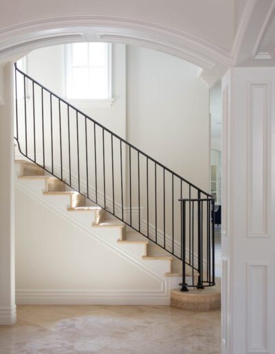 An elegant interior staircase with a black railing, white walls, and steps with natural wood accents.