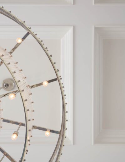 A modern circular chandelier with exposed bulbs mounted on a ceiling with white paneled walls.