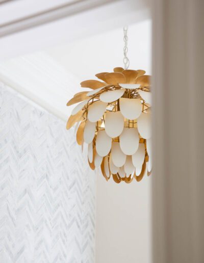 Gold and white pendant light with floral design hanging in a room with herringbone patterned wallpaper.