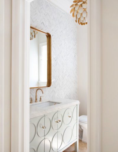 Elegant bathroom interior with herringbone tile wall, ornate vanity, and a gold-framed mirror.