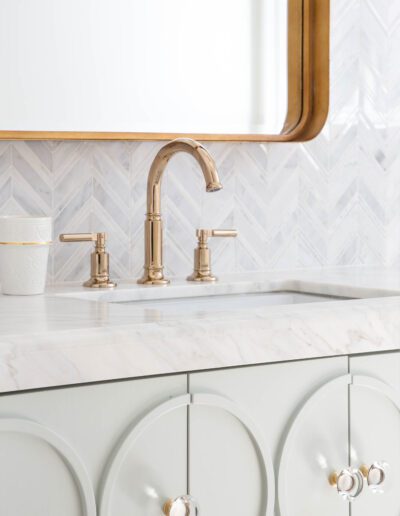 Elegant bathroom vanity with white marble countertop and brass faucet, showcasing a chevron tile backsplash.