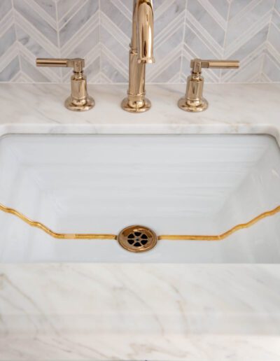 Elegant white rectangular sink with gold trim and matching gold faucet on a marble countertop.