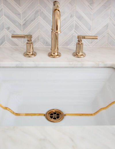 A modern kitchen sink with a white and gold design and a brass faucet, set against a herringbone tile backsplash.