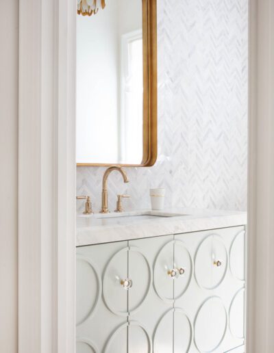 Elegant bathroom vanity with a circular patterned cabinet, brass fixtures, and a herringbone tile backsplash, complemented by a rectangular mirror.