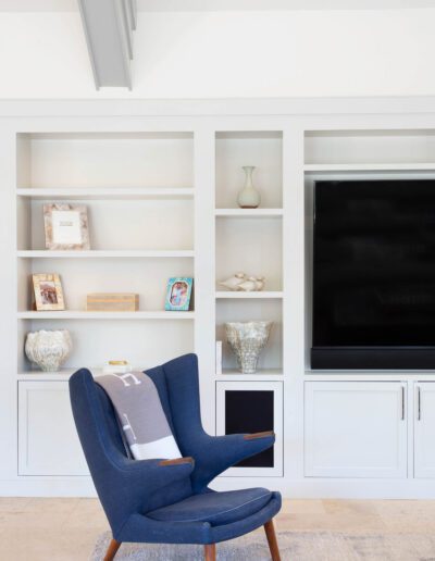 Modern living room with a navy blue armchair, built-in white shelving, decorative items, and a wall-mounted television.