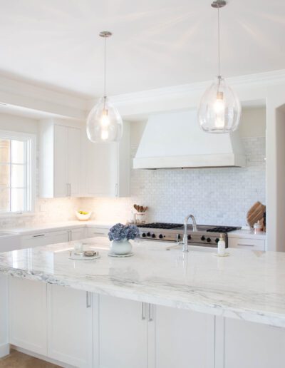 A bright, modern kitchen with white cabinetry, marble countertops, and pendant lighting.