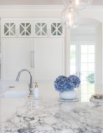 Elegant white kitchen with marble countertops and a bouquet of blue flowers.