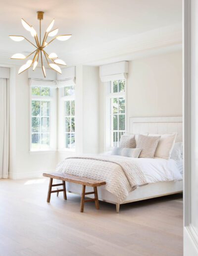 Bright bedroom with modern decor, featuring a white bed, wooden bench, and a starburst chandelier.