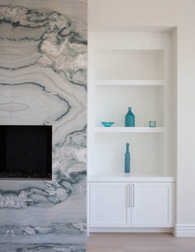 A modern fireplace with marble surround next to a built-in white shelving unit adorned with turquoise decorative items.