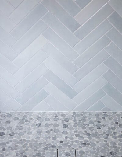 Gray herringbone tile above pebble mosaic tile on a wall.