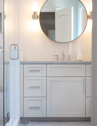 A modern bathroom vanity with a round mirror and white cabinetry.