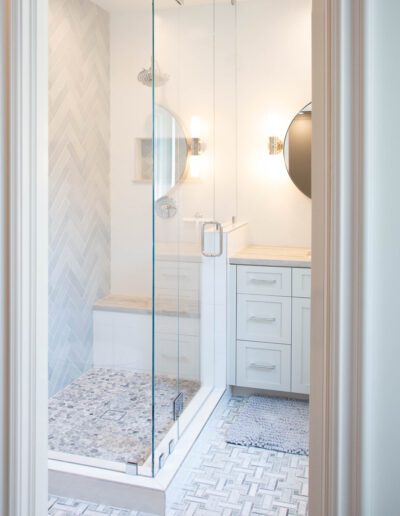 Modern bathroom with herringbone tile pattern and glass shower enclosure.