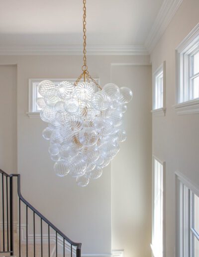 An elegant glass chandelier hanging in a bright stairwell with white walls.