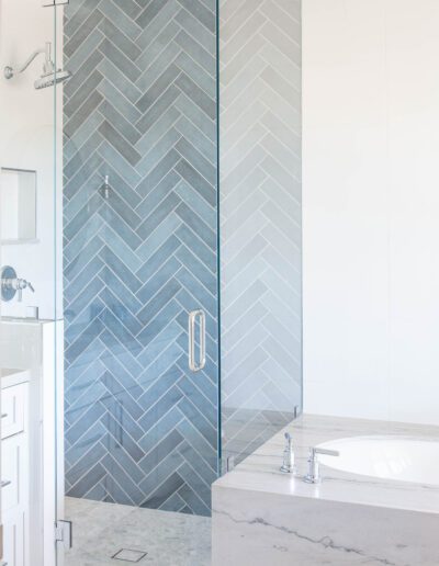 Modern bathroom with a herringbone tiled shower and marble bathtub.