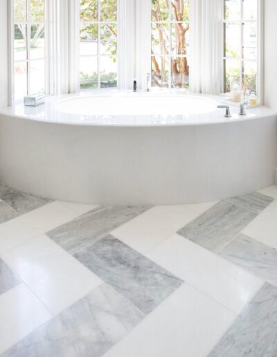 A bright, minimalist bathroom with a white oval bathtub and marble flooring.