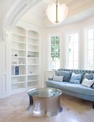 Elegant living room with a blue sofa, white built-in bookshelves, and a metallic coffee table under a chic pendant light.