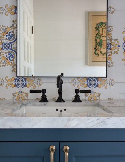 A bathroom vanity with a marble countertop, a rectangular mirror, a modern black faucet, and decorative tiled backsplash in blue, yellow, and white patterns.