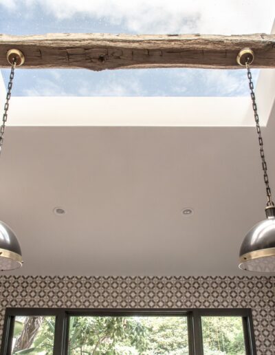 A large skylight with a wooden beam and two hanging pendant lights in a room with patterned walls and built-in shelves.